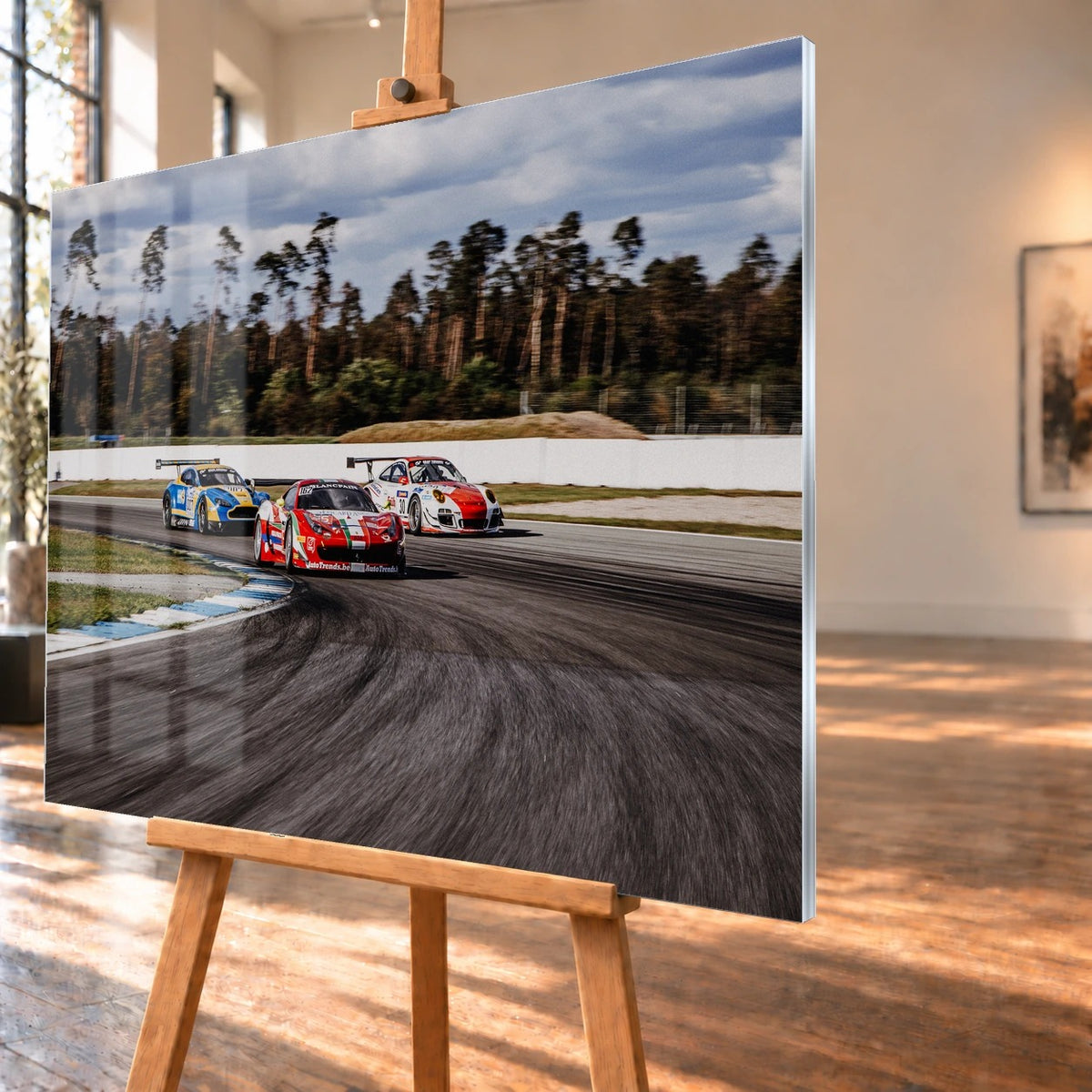 Aston Martin, Porsche und Ferrari GT3 fahren dicht gestaffelt durch eine Kurve; die Mehrwagen-Szene zeigt echtes Renngeschehen. Motiv „Racing Echo“ als Acrylglas-Wandbild, schräg von der Seite auf einer Holzstaffelei.
