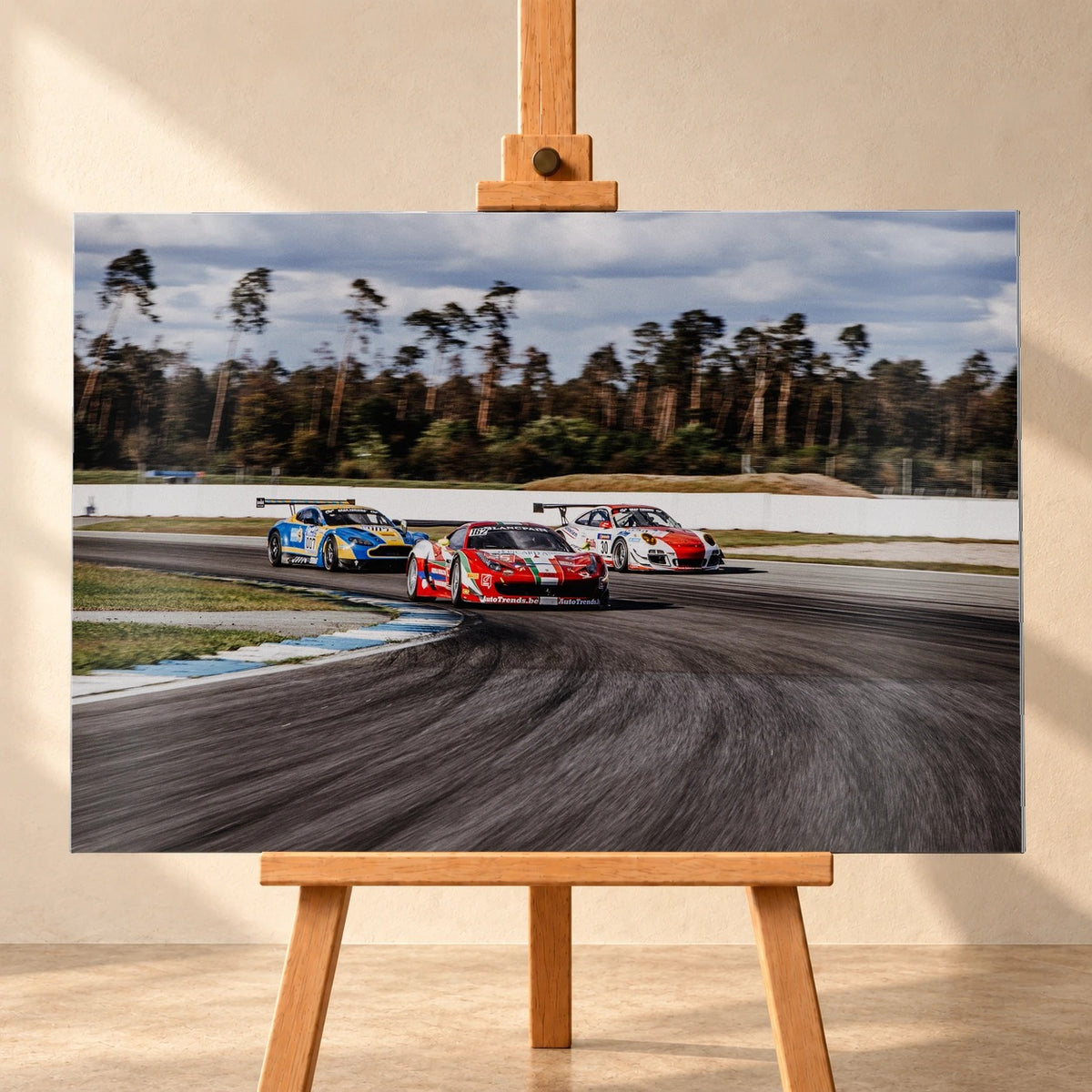 Aston Martin, Porsche und Ferrari GT3 fahren dicht gestaffelt durch eine Kurve; die Mehrwagen-Szene zeigt echtes Renngeschehen. Motiv „Racing Echo“ als Alu gebürstet-Wandbild, frontal auf einer Holzstaffelei.
