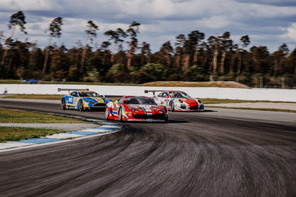 Aston Martin, Porsche und Ferrari GT3 fahren dicht gestaffelt durch eine Kurve; die Mehrwagen-Szene zeigt echtes Renngeschehen. Originalmotiv „Racing Echo“ im Querformat.