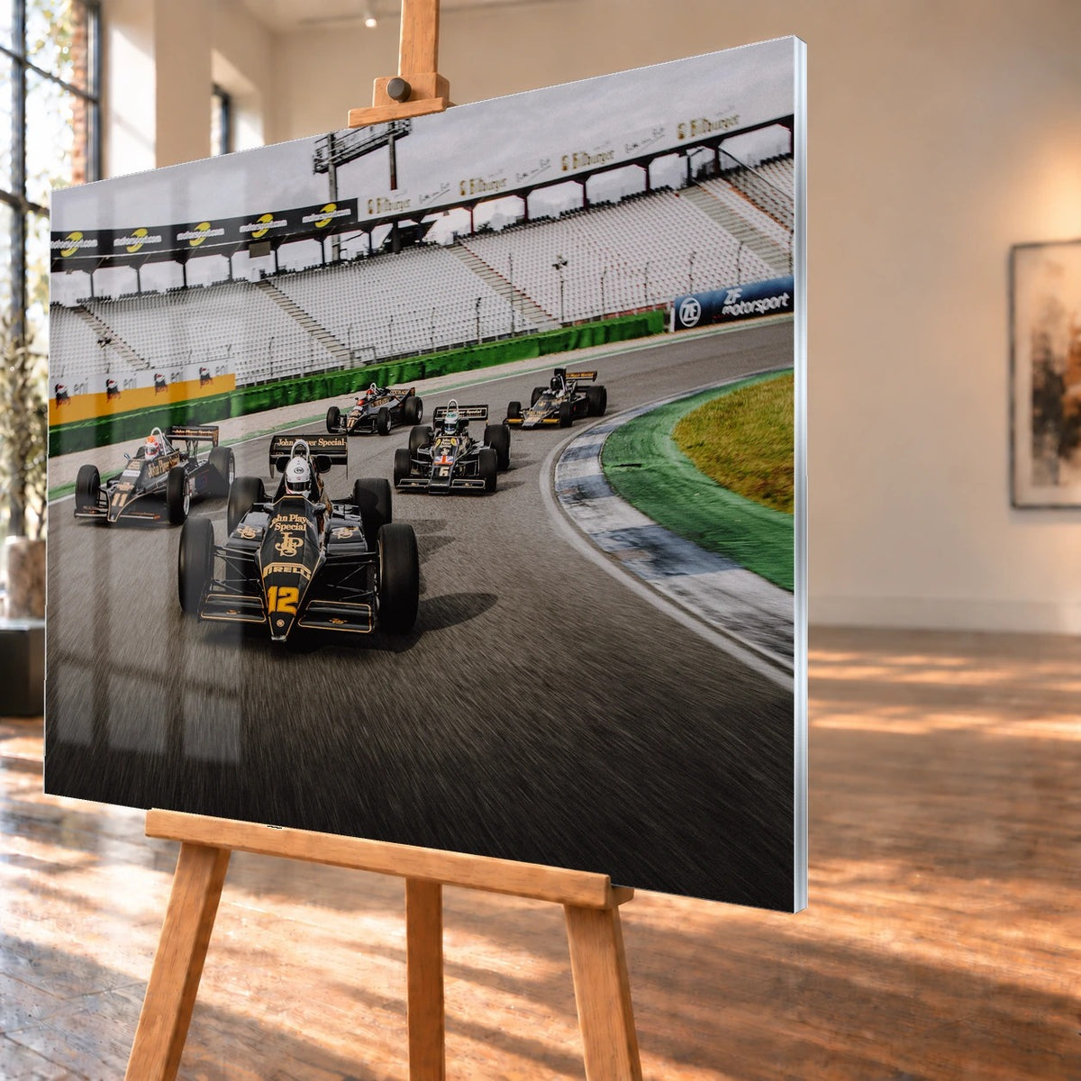 Fünf historische Lotus-Formelwagen fahren als Gruppe durch eine Rennstreckenkurve; schwarze Gold-Lackierungen und Startnummern sind deutlich erkennbar. Motiv „Trackside Story“ als Acrylglas-Wandbild, schräg von der Seite auf einer Holzstaffelei.