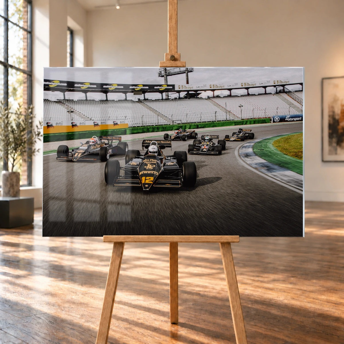 Fünf historische Lotus-Formelwagen fahren als Gruppe durch eine Rennstreckenkurve; schwarze Gold-Lackierungen und Startnummern sind deutlich erkennbar. Motiv „Trackside Story“ als Acrylglas-Wandbild, auf einer Holzstaffelei in einem hellen Galerieraum.