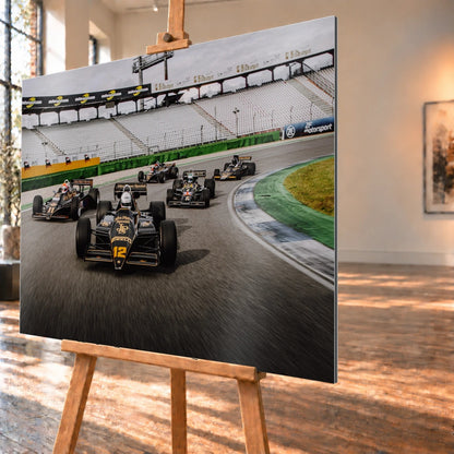 Fünf historische Lotus-Formelwagen fahren als Gruppe durch eine Rennstreckenkurve; schwarze Gold-Lackierungen und Startnummern sind deutlich erkennbar. Motiv „Trackside Story“ als Alu gebürstet-Wandbild, schräg von der Seite auf einer Holzstaffelei.