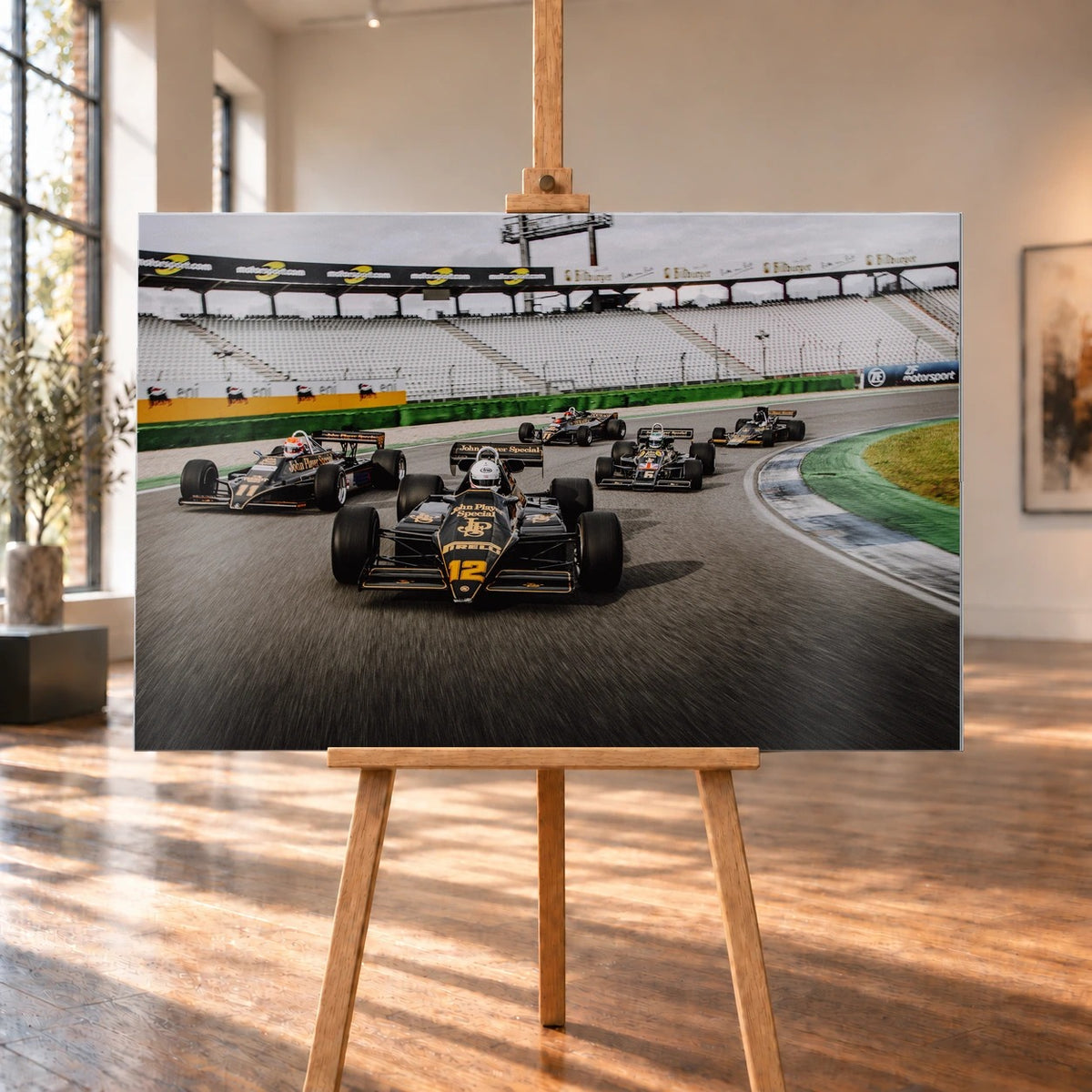 Fünf historische Lotus-Formelwagen fahren als Gruppe durch eine Rennstreckenkurve; schwarze Gold-Lackierungen und Startnummern sind deutlich erkennbar. Motiv „Trackside Story“ als Alu gebürstet-Wandbild, auf einer Holzstaffelei in einem hellen Galerieraum.