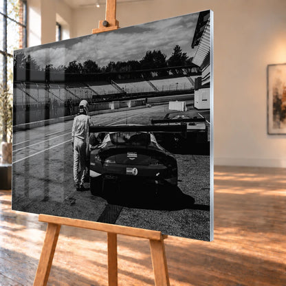 Der Aston Martin Vantage V12 GT3 Billy steht von hinten in der Boxengasse; eine Person lehnt am geöffneten Heckbereich und gibt dem Bild Maßstab. Motiv „Racing Frame“ als Acrylglas-Wandbild, schräg von der Seite auf einer Holzstaffelei.
