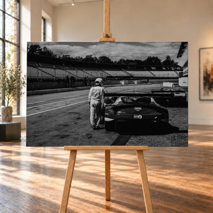 Der Aston Martin Vantage V12 GT3 Billy steht von hinten in der Boxengasse; eine Person lehnt am geöffneten Heckbereich und gibt dem Bild Maßstab. Motiv „Racing Frame“ als Leinwand-Wandbild, auf einer Holzstaffelei in einem hellen Galerieraum.