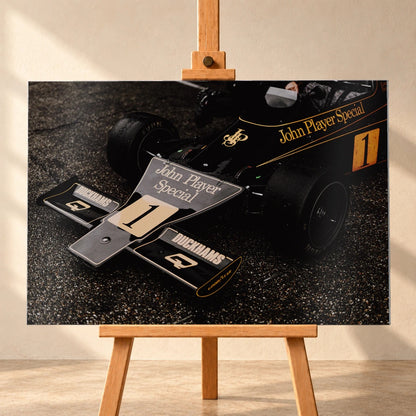 Die Nahaufnahme zeigt die spitze Front des Lotus 76 mit goldener John-Player-Special-Lackierung und großer Startnummer 1. Motiv „Apex Story“ als Alu gebürstet-Wandbild, frontal auf einer Holzstaffelei.