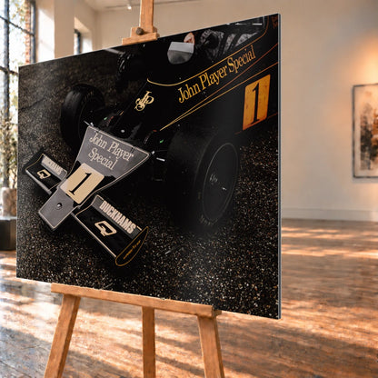 Die Nahaufnahme zeigt die spitze Front des Lotus 76 mit goldener John-Player-Special-Lackierung und großer Startnummer 1. Motiv „Apex Story“ als Alu gebürstet-Wandbild, schräg von der Seite auf einer Holzstaffelei.