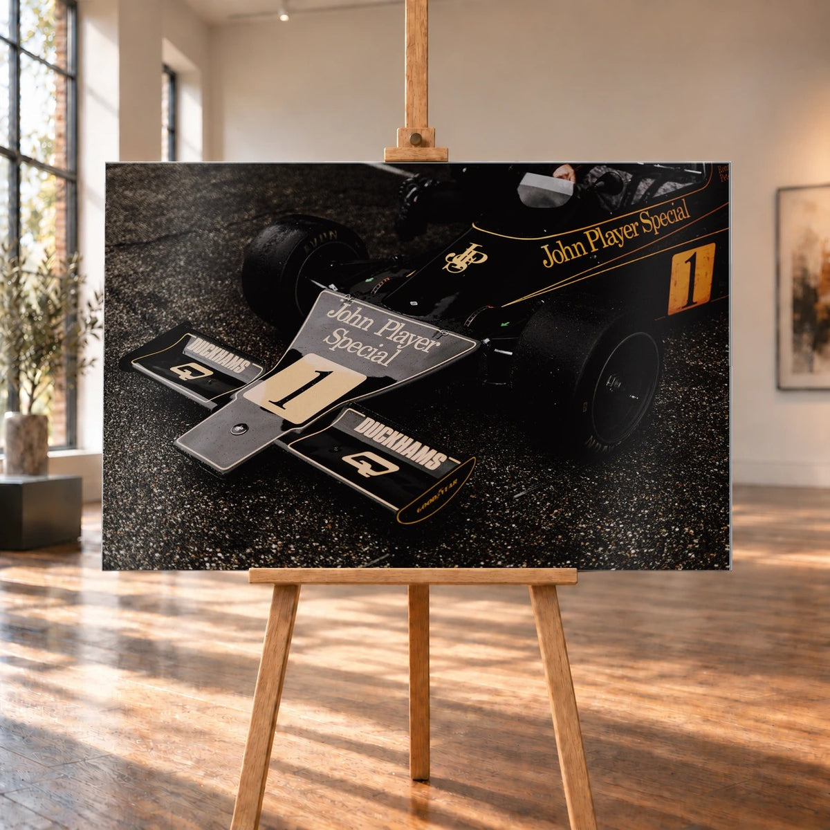 Die Nahaufnahme zeigt die spitze Front des Lotus 76 mit goldener John-Player-Special-Lackierung und großer Startnummer 1. Motiv „Apex Story“ als Alu gebürstet-Wandbild, auf einer Holzstaffelei in einem hellen Galerieraum.