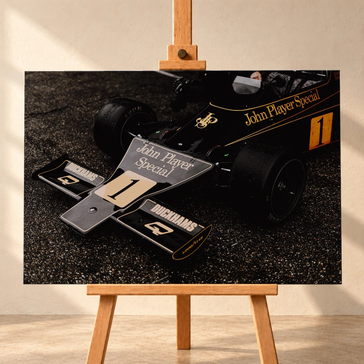 Die Nahaufnahme zeigt die spitze Front des Lotus 76 mit goldener John-Player-Special-Lackierung und großer Startnummer 1. Motiv „Apex Story“ als Leinwand-Wandbild, frontal auf einer Holzstaffelei.