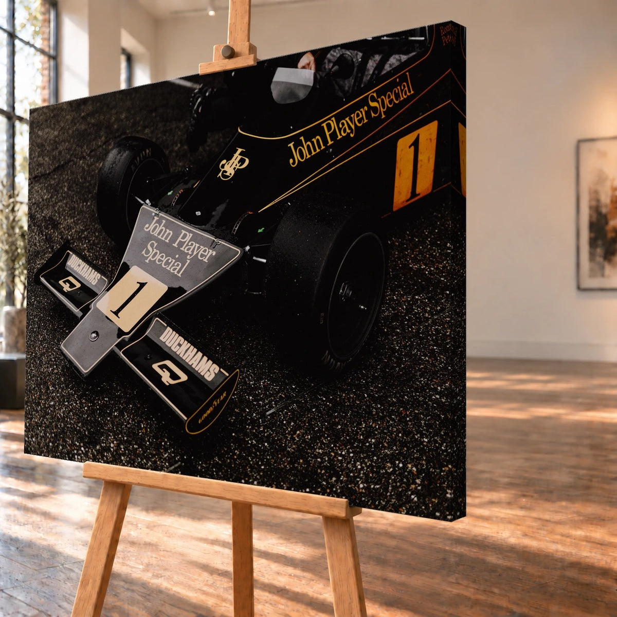 Die Nahaufnahme zeigt die spitze Front des Lotus 76 mit goldener John-Player-Special-Lackierung und großer Startnummer 1. Motiv „Apex Story“ als Leinwand-Wandbild, schräg von der Seite auf einer Holzstaffelei.
