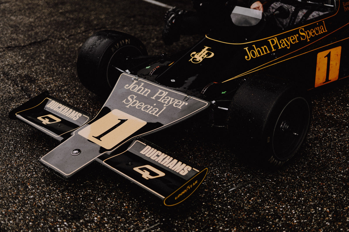 Die Nahaufnahme zeigt die spitze Front des Lotus 76 mit goldener John-Player-Special-Lackierung und großer Startnummer 1. Originalmotiv „Apex Story“ im Querformat.