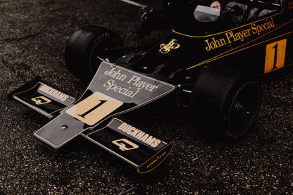Die Nahaufnahme zeigt die spitze Front des Lotus 76 mit goldener John-Player-Special-Lackierung und großer Startnummer 1. Originalmotiv „Apex Story“ im Querformat.