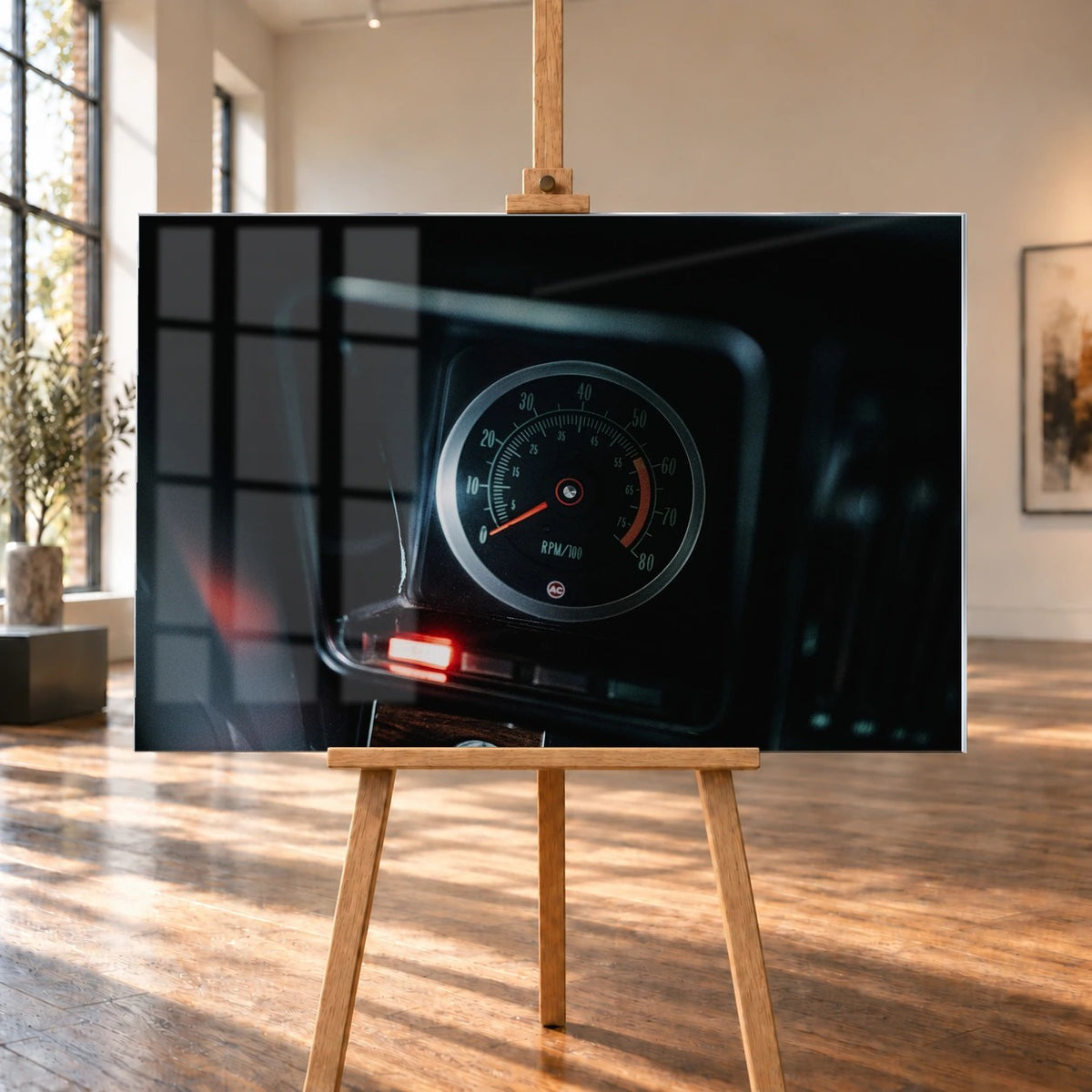 Ein einzelner Rundinstrument-Zähler leuchtet im dunklen Innenraum des Camaro Yenko; rote Kontrollleuchte und Skala sind klar sichtbar. Motiv „Silver Moment“ als Acrylglas-Wandbild, auf einer Holzstaffelei in einem hellen Galerieraum.