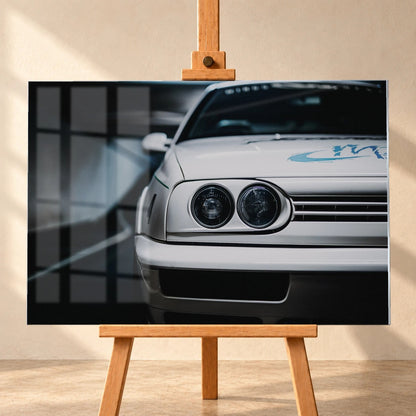 Die Frontpartie von Jesses Jetta ist eng angeschnitten; zwei runde Scheinwerfer und die graue Grafik auf weißem Lack bestimmen das Bild. Motiv „Silver Horizon“ als Acrylglas-Wandbild, frontal auf einer Holzstaffelei.