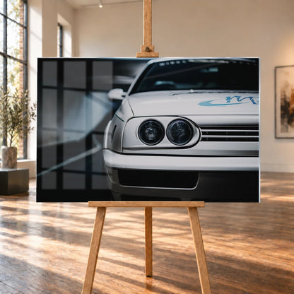 Die Frontpartie von Jesses Jetta ist eng angeschnitten; zwei runde Scheinwerfer und die graue Grafik auf weißem Lack bestimmen das Bild. Motiv „Silver Horizon“ als Acrylglas-Wandbild, auf einer Holzstaffelei in einem hellen Galerieraum.