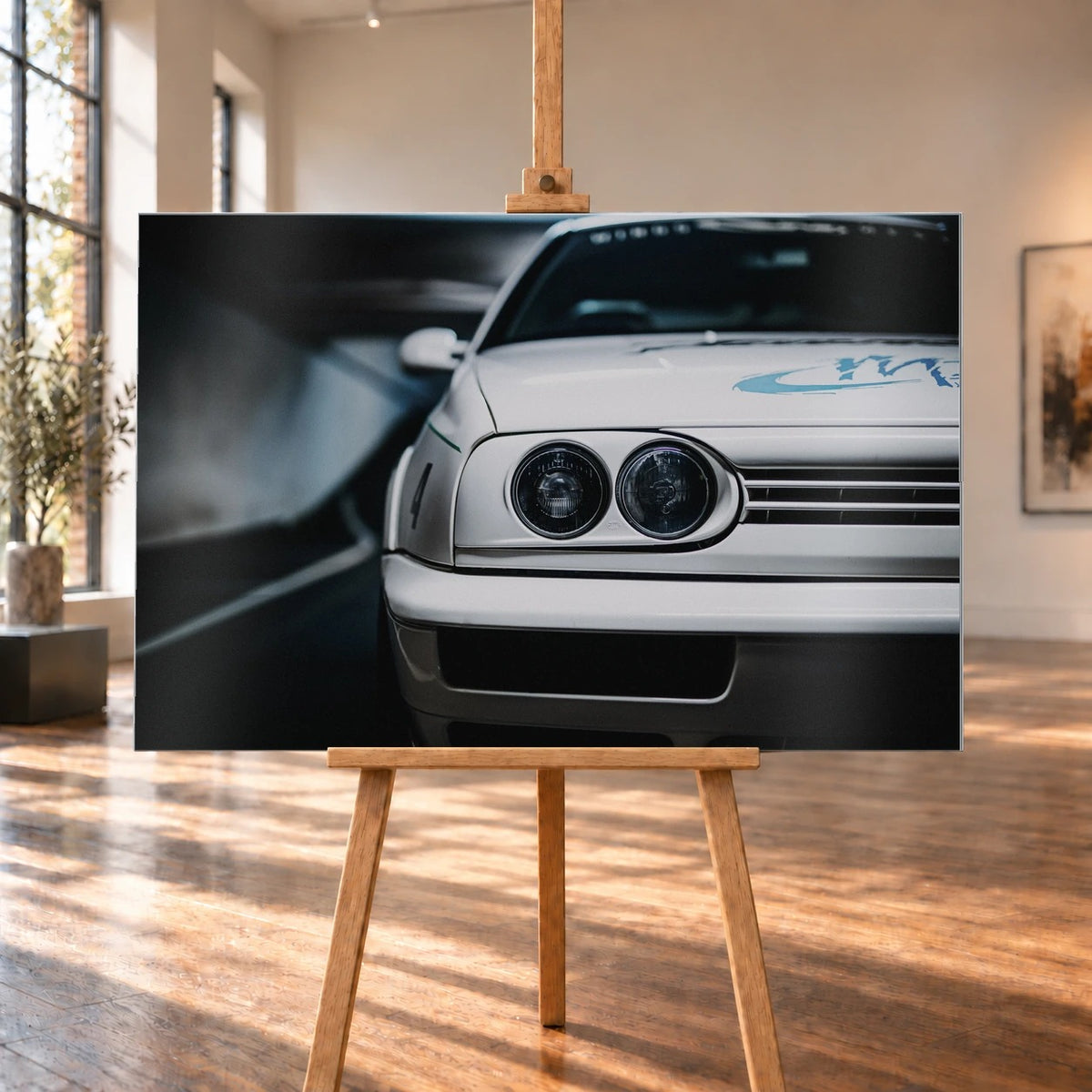 Die Frontpartie von Jesses Jetta ist eng angeschnitten; zwei runde Scheinwerfer und die graue Grafik auf weißem Lack bestimmen das Bild. Motiv „Silver Horizon“ als Alu gebürstet-Wandbild, auf einer Holzstaffelei in einem hellen Galerieraum.
