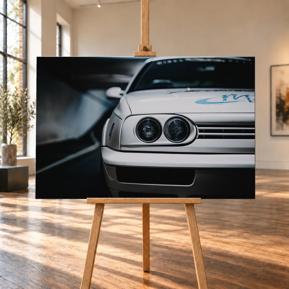 Die Frontpartie von Jesses Jetta ist eng angeschnitten; zwei runde Scheinwerfer und die graue Grafik auf weißem Lack bestimmen das Bild. Motiv „Silver Horizon“ als Leinwand-Wandbild, auf einer Holzstaffelei in einem hellen Galerieraum.