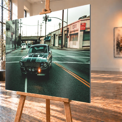 Eleanor fährt frontal über eine leere Stadtstraße; Laternen, Industriegebäude und kühles Morgenlicht rahmen die Doppelstreifen ein. Motiv „Screen Echo 2“ als Alu gebürstet-Wandbild, schräg von der Seite auf einer Holzstaffelei.