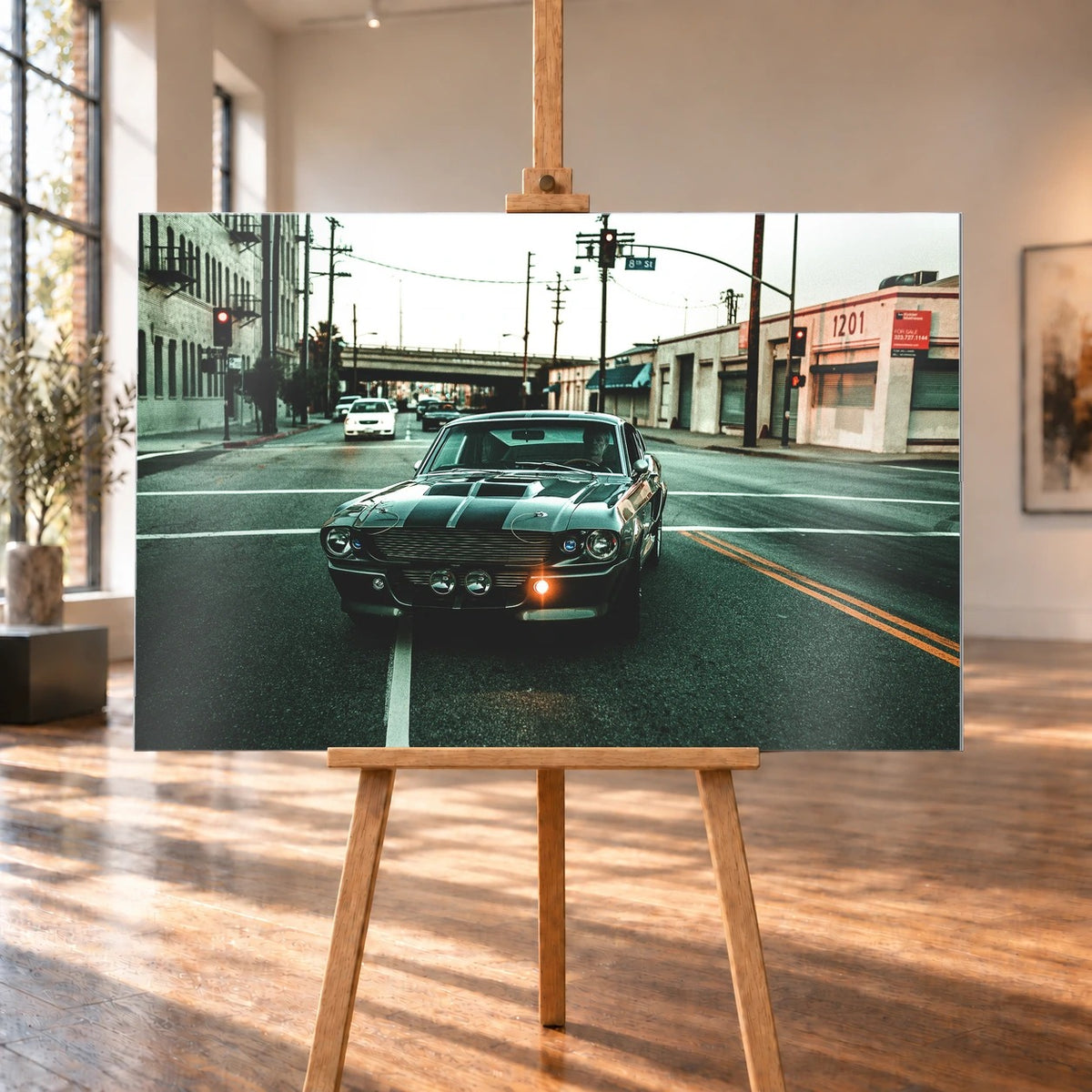 Eleanor fährt frontal über eine leere Stadtstraße; Laternen, Industriegebäude und kühles Morgenlicht rahmen die Doppelstreifen ein. Motiv „Screen Echo 2“ als Alu gebürstet-Wandbild, auf einer Holzstaffelei in einem hellen Galerieraum.