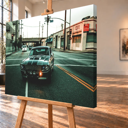 Eleanor fährt frontal über eine leere Stadtstraße; Laternen, Industriegebäude und kühles Morgenlicht rahmen die Doppelstreifen ein. Motiv „Screen Echo 2“ als Leinwand-Wandbild, schräg von der Seite auf einer Holzstaffelei.