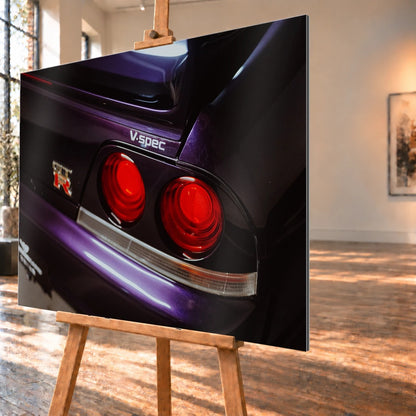 Eine enge Heckaufnahme zeigt zwei rote Rundlichter, GT-R- und V-Spec-Schriftzug sowie den violetten Lack des Nissan Skyline R33. Motiv „Neon Presence“ als Alu gebürstet-Wandbild, schräg von der Seite auf einer Holzstaffelei.