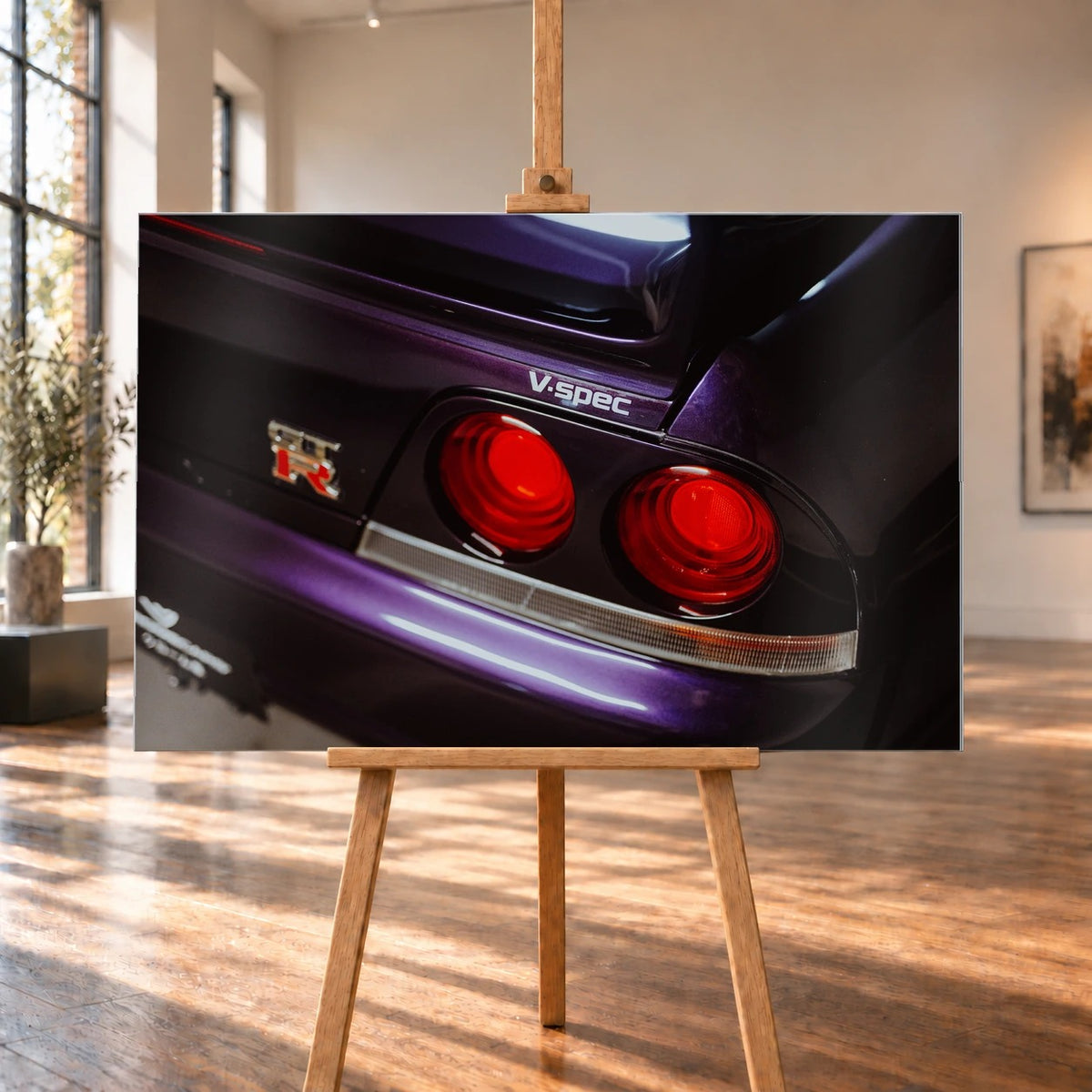 Eine enge Heckaufnahme zeigt zwei rote Rundlichter, GT-R- und V-Spec-Schriftzug sowie den violetten Lack des Nissan Skyline R33. Motiv „Neon Presence“ als Alu gebürstet-Wandbild, auf einer Holzstaffelei in einem hellen Galerieraum.