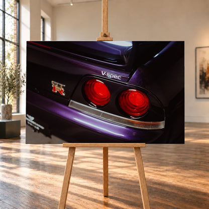 Eine enge Heckaufnahme zeigt zwei rote Rundlichter, GT-R- und V-Spec-Schriftzug sowie den violetten Lack des Nissan Skyline R33. Motiv „Neon Presence“ als Leinwand-Wandbild, auf einer Holzstaffelei in einem hellen Galerieraum.