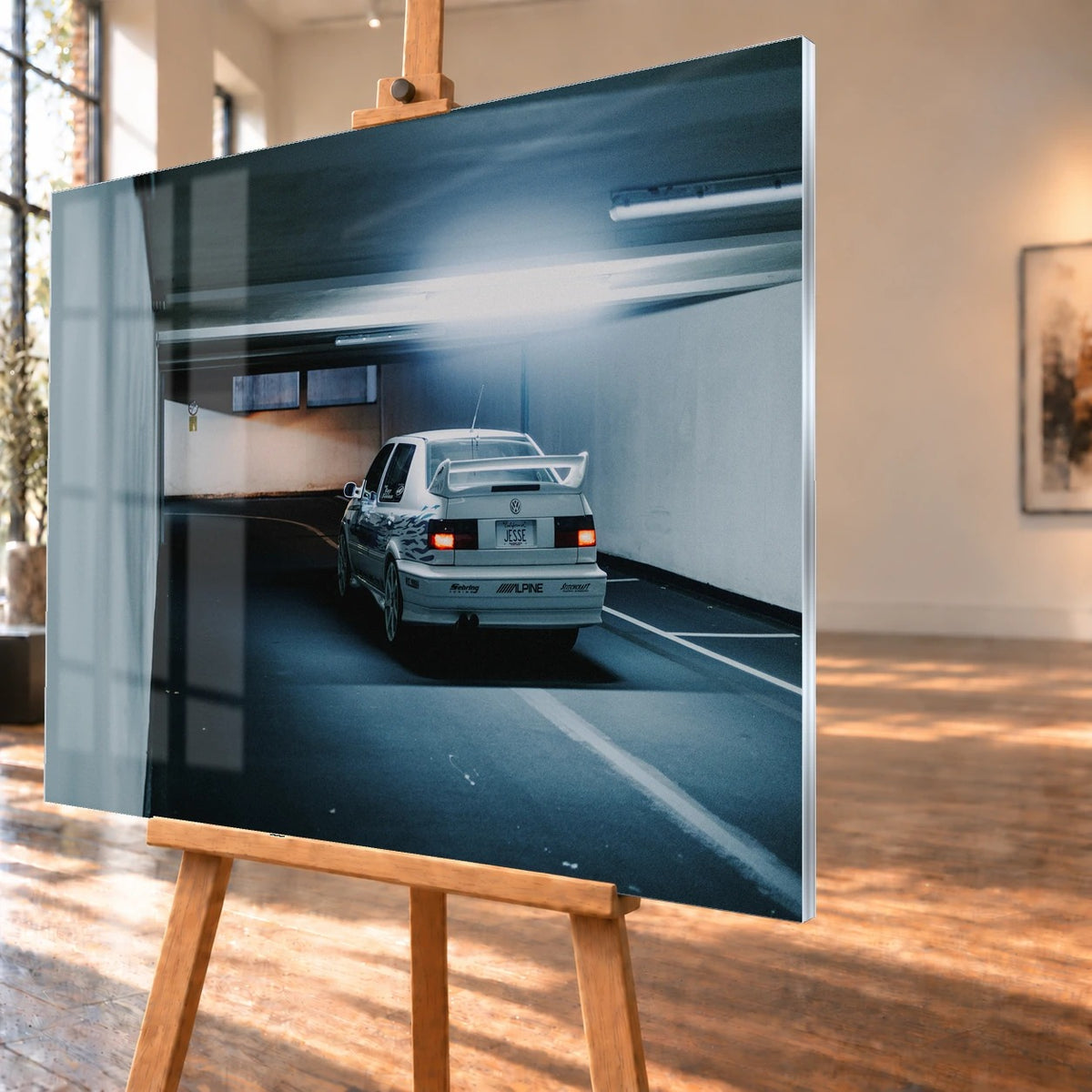Jesses Jetta ist von hinten in einer langen Parkhausspur aufgenommen; die weiße Karosserie hebt sich klein vom kühlen Tunnel ab. Motiv „Screen Presence“ als Acrylglas-Wandbild, schräg von der Seite auf einer Holzstaffelei.