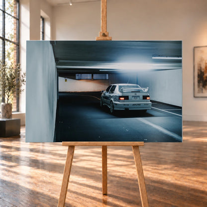 Jesses Jetta ist von hinten in einer langen Parkhausspur aufgenommen; die weiße Karosserie hebt sich klein vom kühlen Tunnel ab. Motiv „Screen Presence“ als Alu gebürstet-Wandbild, auf einer Holzstaffelei in einem hellen Galerieraum.