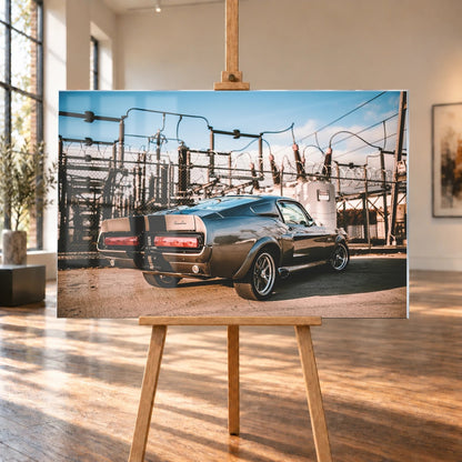 Eleanor steht schräg von hinten vor einem Umspannwerk; Masten, Leitungen und warme Sonne bilden einen technischen Hintergrund. Motiv „Road Moment“ als Acrylglas-Wandbild, auf einer Holzstaffelei in einem hellen Galerieraum.