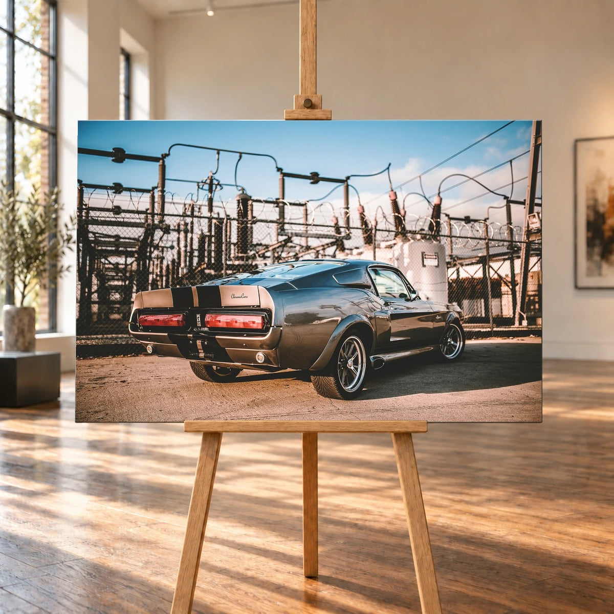 Eleanor steht schräg von hinten vor einem Umspannwerk; Masten, Leitungen und warme Sonne bilden einen technischen Hintergrund. Motiv „Road Moment“ als Leinwand-Wandbild, auf einer Holzstaffelei in einem hellen Galerieraum.