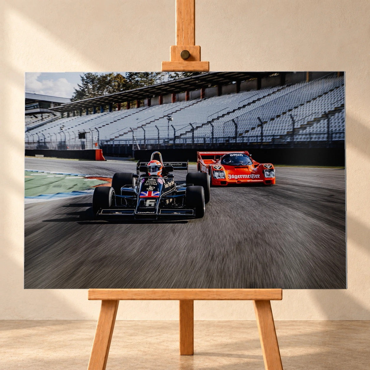 Lotus 77 und der Porsche 962 Brun/Jägermeister fahren nebeneinander beziehungsweise versetzt über die Strecke; orange und schwarz setzen klare Rennfarben. Motiv „Grid Rhythm“ als Alu gebürstet-Wandbild, frontal auf einer Holzstaffelei.