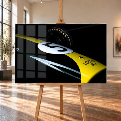 Eine enge, fast abstrakte Detailaufnahme zeigt grün-gelbe Lotus-49-Lackierung, weiße Startnummer und Reifenflanke vor schwarzem Hintergrund. Motiv „Fast Moment“ als Acrylglas-Wandbild, auf einer Holzstaffelei in einem hellen Galerieraum.