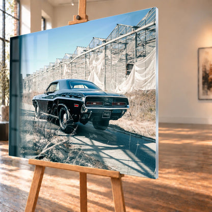 Der schwarze Dodge Challenger ist schräg von hinten auf einem Industriegelände aufgenommen; breite Karosserie und rote Rückleuchten wirken kraftvoll. Motiv „Timeless Pulse“ als Acrylglas-Wandbild, schräg von der Seite auf einer Holzstaffelei.