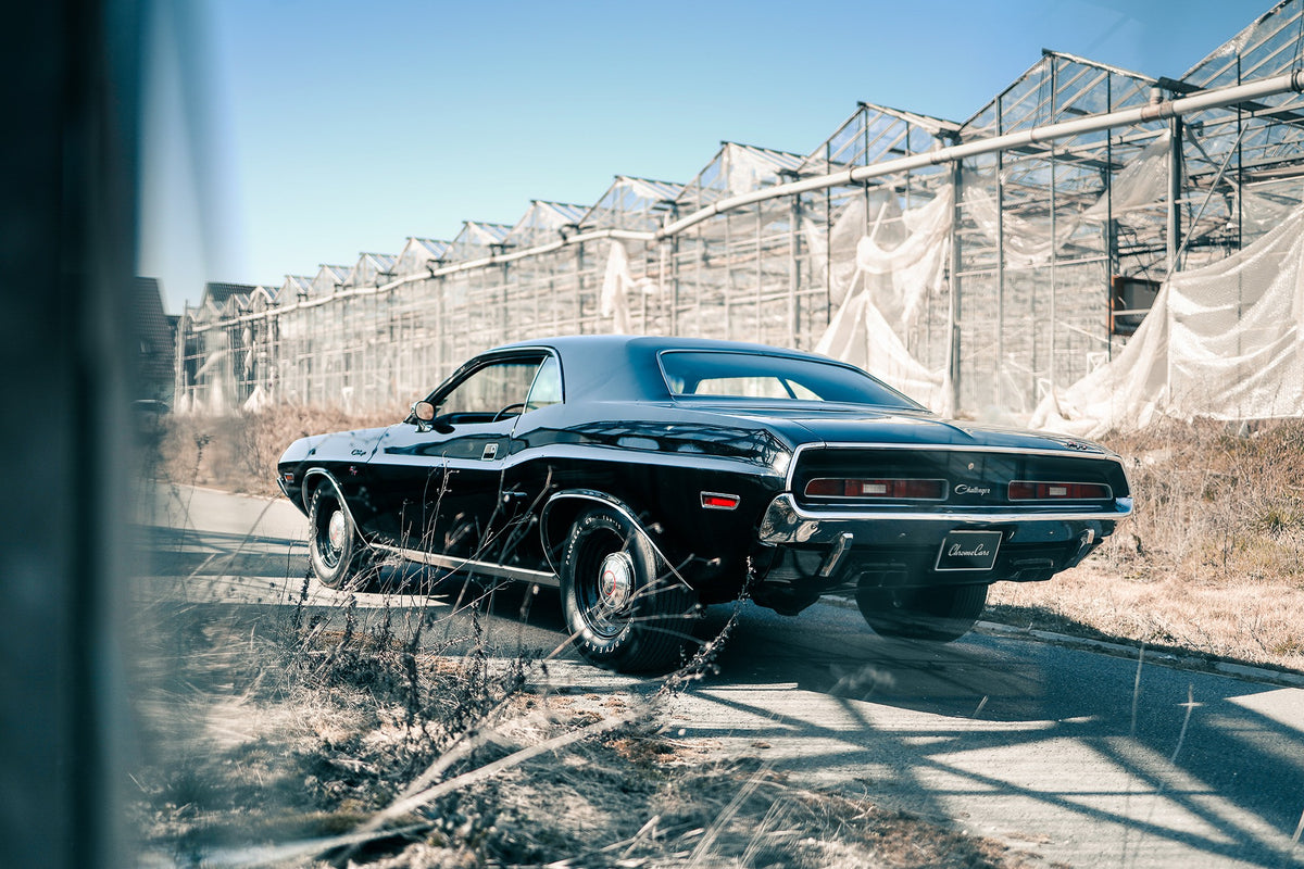 Der schwarze Dodge Challenger ist schräg von hinten auf einem Industriegelände aufgenommen; breite Karosserie und rote Rückleuchten wirken kraftvoll. Originalmotiv „Timeless Pulse“ im Querformat.