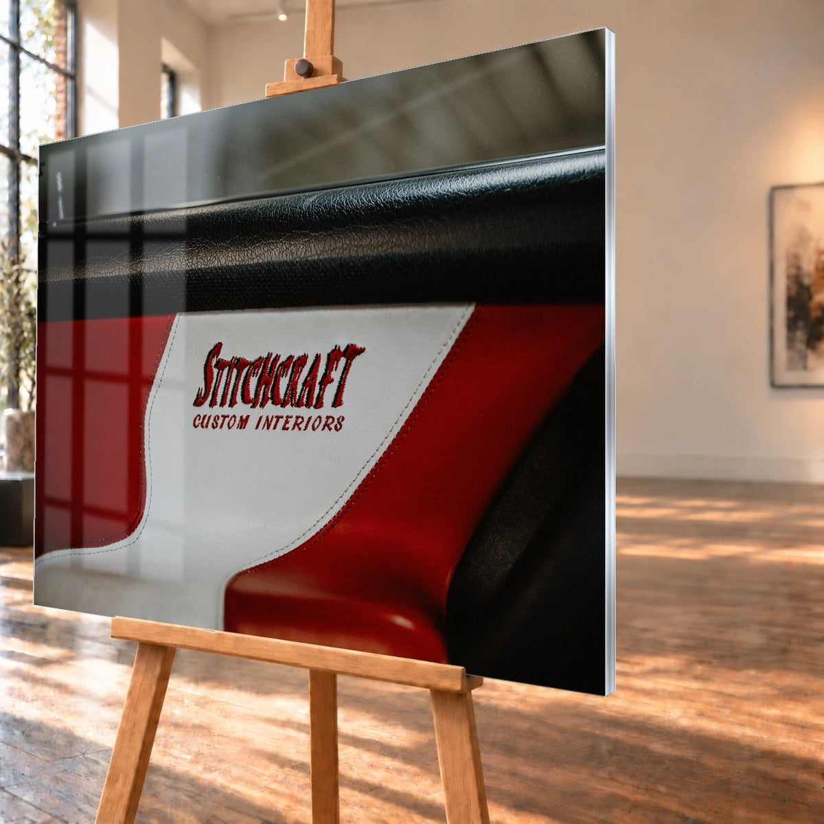 Die Nahaufnahme zeigt den rot-weißen Innenraumbezug mit Stitchcraft-Schriftzug; Material, Naht und Farbe stehen im Mittelpunkt. Motiv „Cinematic Horizon“ als Acrylglas-Wandbild, schräg von der Seite auf einer Holzstaffelei.