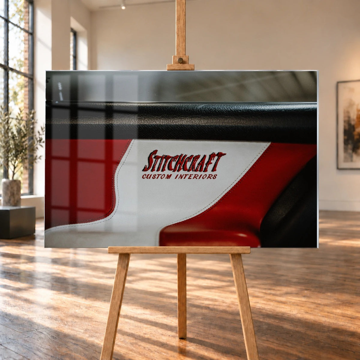 Die Nahaufnahme zeigt den rot-weißen Innenraumbezug mit Stitchcraft-Schriftzug; Material, Naht und Farbe stehen im Mittelpunkt. Motiv „Cinematic Horizon“ als Acrylglas-Wandbild, auf einer Holzstaffelei in einem hellen Galerieraum.