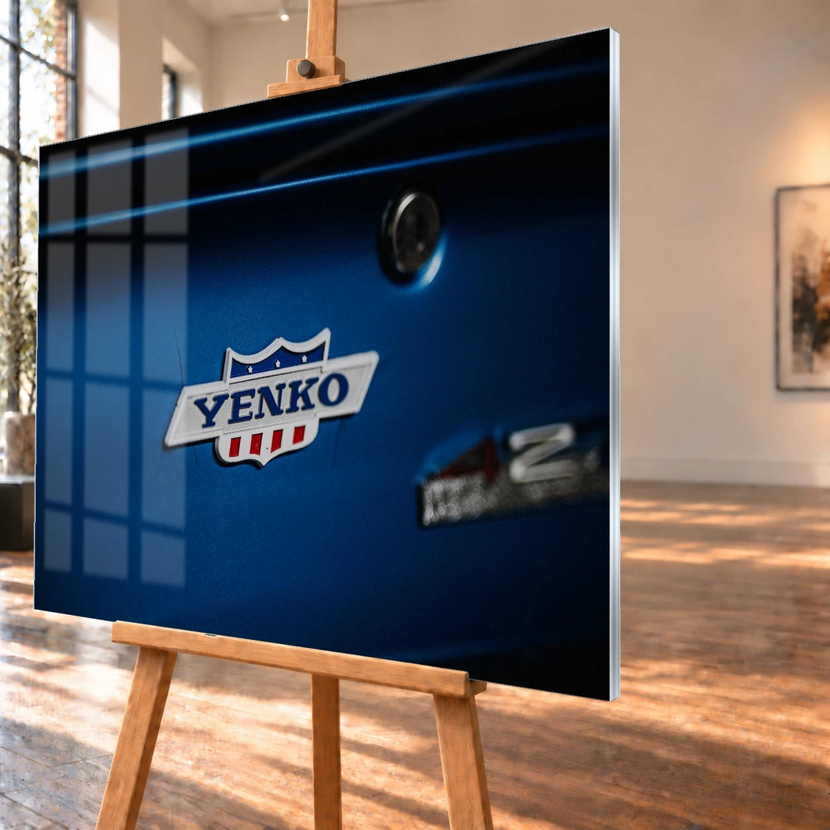 Das Yenko-Emblem sitzt als helles Detail auf der blauen Karosserie; Lack, Chrom und Schriftzug füllen die Aufnahme. Motiv „Hero Line“ als Acrylglas-Wandbild, schräg von der Seite auf einer Holzstaffelei.