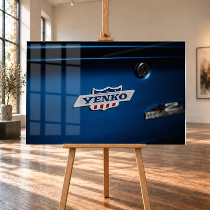 Das Yenko-Emblem sitzt als helles Detail auf der blauen Karosserie; Lack, Chrom und Schriftzug füllen die Aufnahme. Motiv „Hero Line“ als Acrylglas-Wandbild, auf einer Holzstaffelei in einem hellen Galerieraum.
