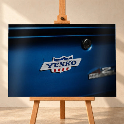 Das Yenko-Emblem sitzt als helles Detail auf der blauen Karosserie; Lack, Chrom und Schriftzug füllen die Aufnahme. Motiv „Hero Line“ als Alu gebürstet-Wandbild, frontal auf einer Holzstaffelei.