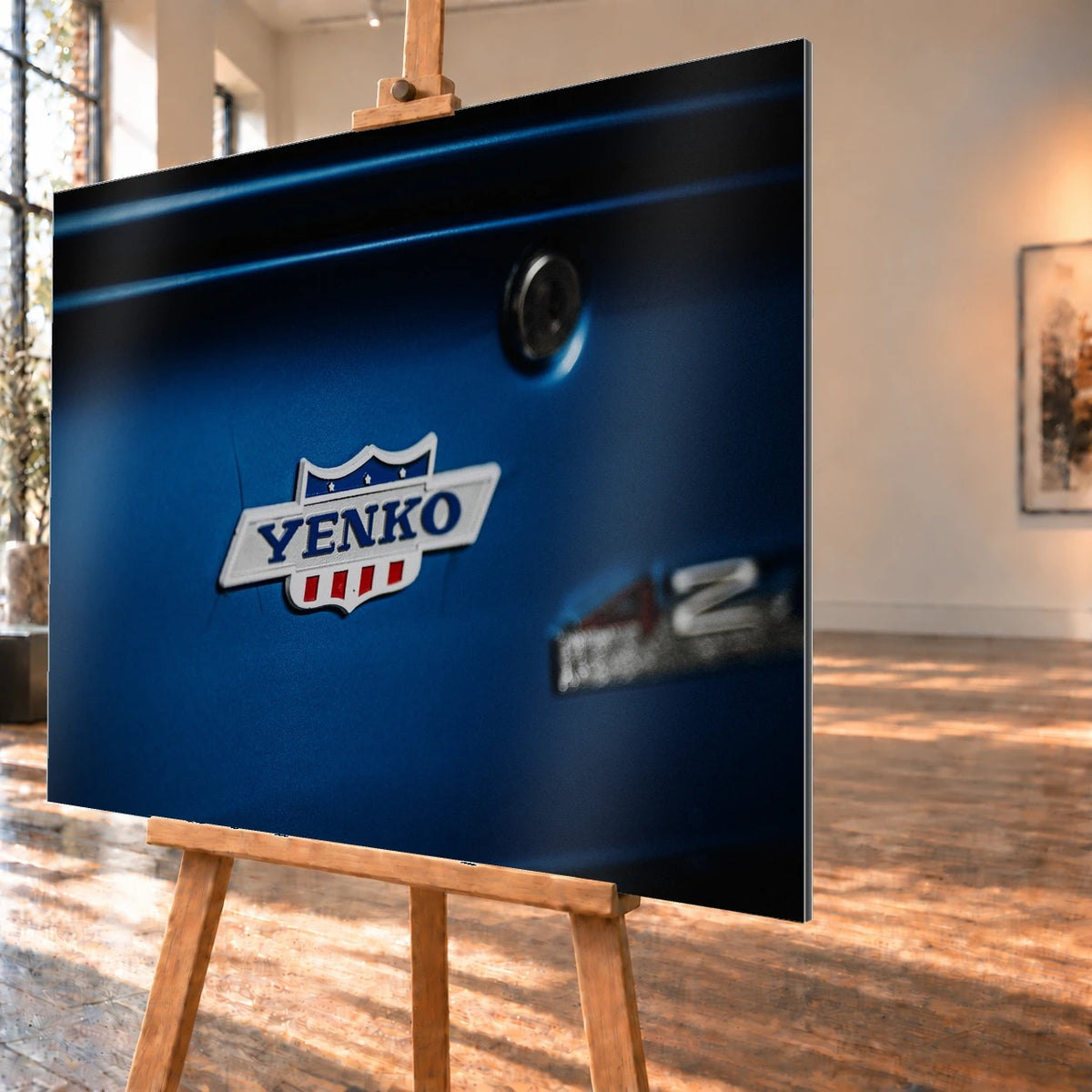 Das Yenko-Emblem sitzt als helles Detail auf der blauen Karosserie; Lack, Chrom und Schriftzug füllen die Aufnahme. Motiv „Hero Line“ als Alu gebürstet-Wandbild, schräg von der Seite auf einer Holzstaffelei.