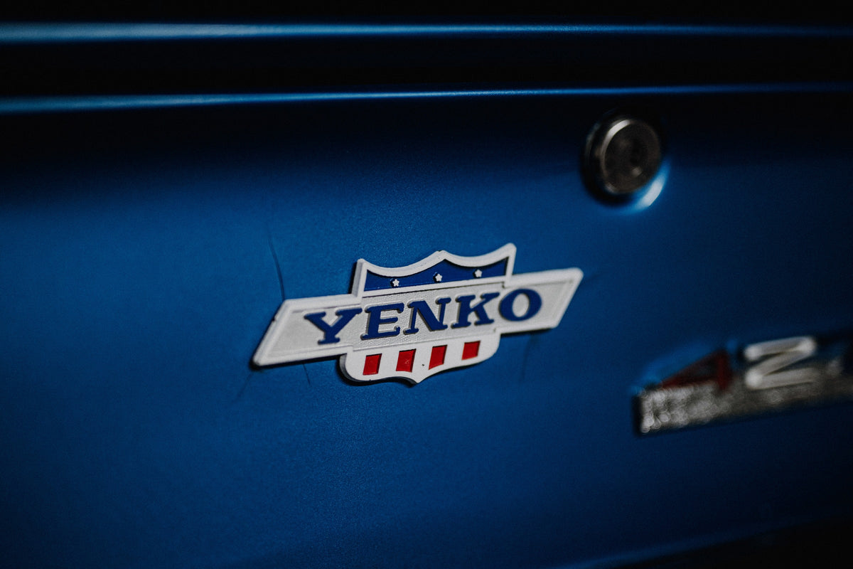 Das Yenko-Emblem sitzt als helles Detail auf der blauen Karosserie; Lack, Chrom und Schriftzug füllen die Aufnahme. Originalmotiv „Hero Line“ im Querformat.