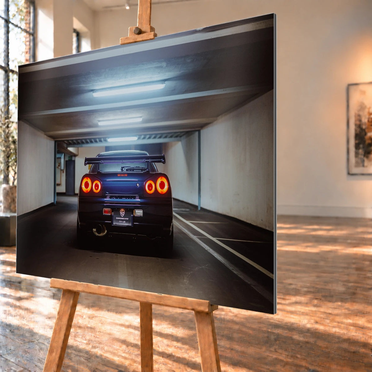 Der Nissan Skyline R34 ist exakt mittig von hinten aufgenommen; vier leuchtende Rundlichter und die geraden Parkhauslinien rahmen ihn ein. Motiv „Neon Rhythm“ als Alu gebürstet-Wandbild, schräg von der Seite auf einer Holzstaffelei.