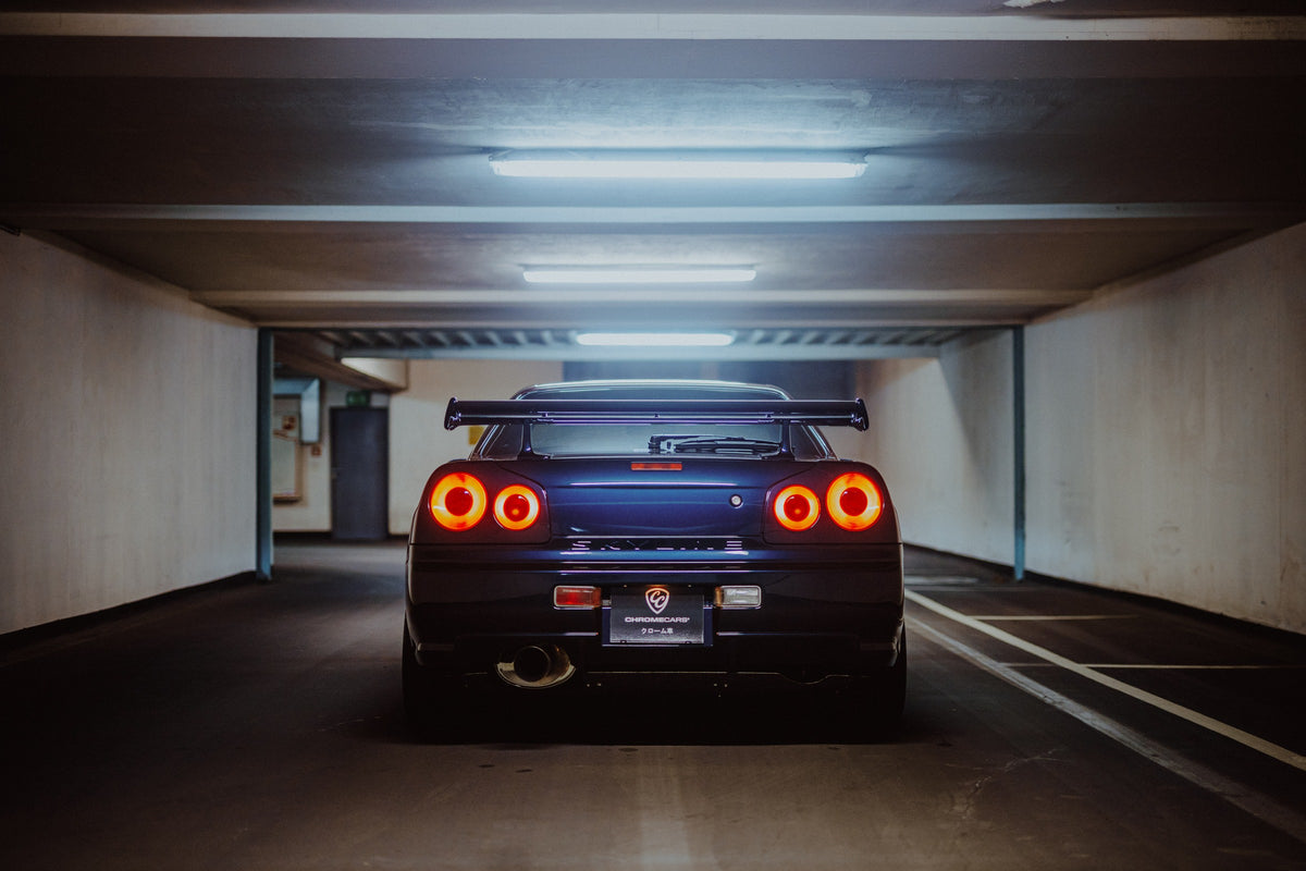 Der Nissan Skyline R34 ist exakt mittig von hinten aufgenommen; vier leuchtende Rundlichter und die geraden Parkhauslinien rahmen ihn ein. Originalmotiv „Neon Rhythm“ im Querformat.