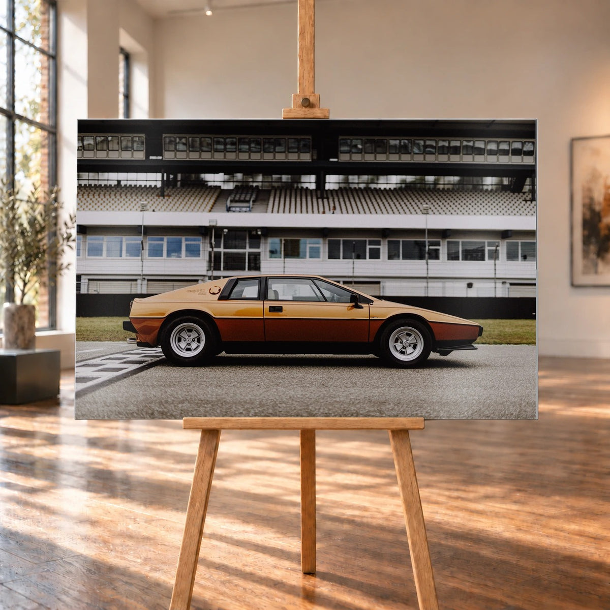 Der goldene Lotus Esprit steht streng im Seitenprofil vor der Boxenanlage; Keilform und dunkle Räder zeichnen eine klare Silhouette. Motiv „Timeless Rhythm“ als Alu gebürstet-Wandbild, auf einer Holzstaffelei in einem hellen Galerieraum.