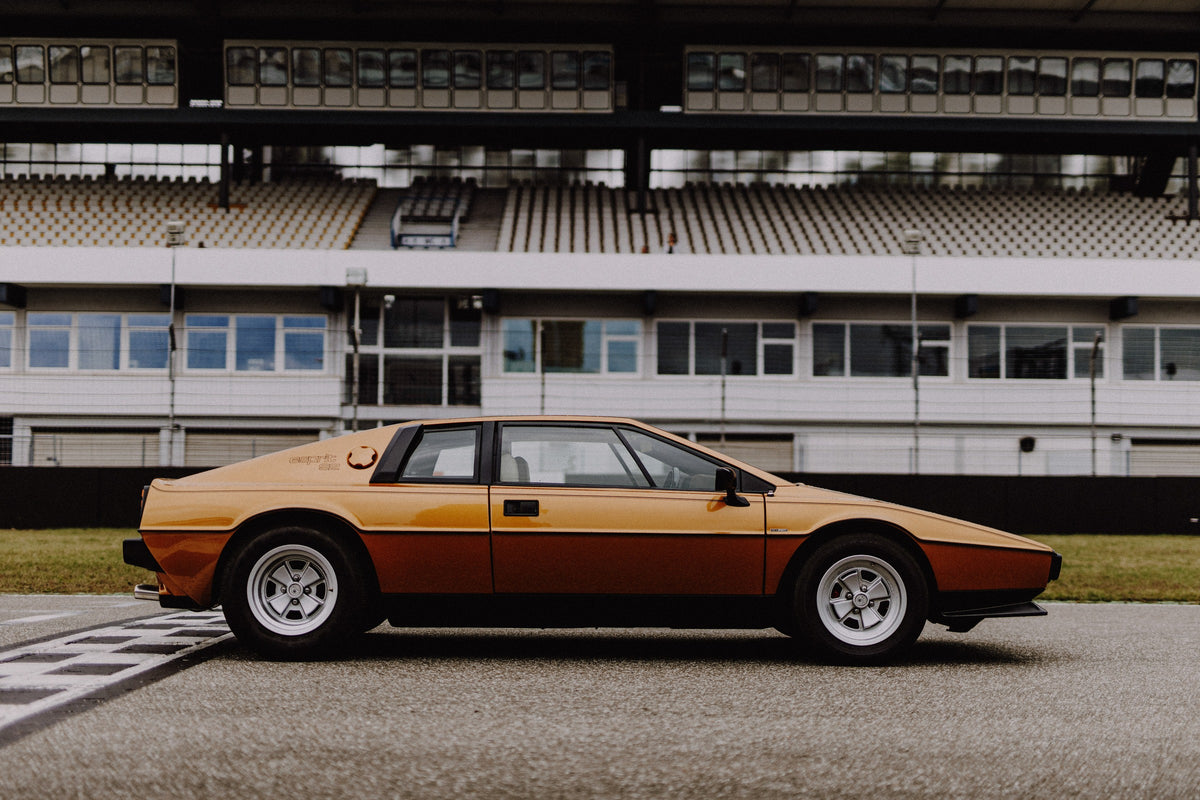 Der goldene Lotus Esprit steht streng im Seitenprofil vor der Boxenanlage; Keilform und dunkle Räder zeichnen eine klare Silhouette. Originalmotiv „Timeless Rhythm“ im Querformat.