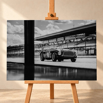 Der MG Tojeiro steht im Schwarz-Weiß-Seitenprofil vor der Boxenanlage; sein Spiegelbild erscheint auf dem nassen Boden. Motiv „Trackside Echo“ als Leinwand-Wandbild, frontal auf einer Holzstaffelei.