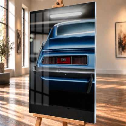 Das Heck des blauen Camaro Yenko ist eng angeschnitten; Rücklicht, Spoilerkante und schwarze Blende bilden horizontale Flächen. Motiv „Screen Focus“ als Acrylglas-Wandbild, schräg von der Seite auf einer Holzstaffelei.