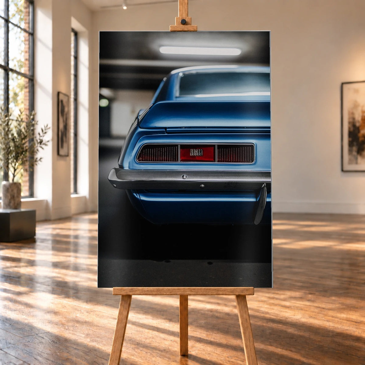 Das Heck des blauen Camaro Yenko ist eng angeschnitten; Rücklicht, Spoilerkante und schwarze Blende bilden horizontale Flächen. Motiv „Screen Focus“ als Alu gebürstet-Wandbild, auf einer Holzstaffelei in einem hellen Galerieraum.