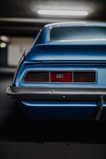 Das Heck des blauen Camaro Yenko ist eng angeschnitten; Rücklicht, Spoilerkante und schwarze Blende bilden horizontale Flächen. Originalmotiv „Screen Focus“ im Hochformat.
